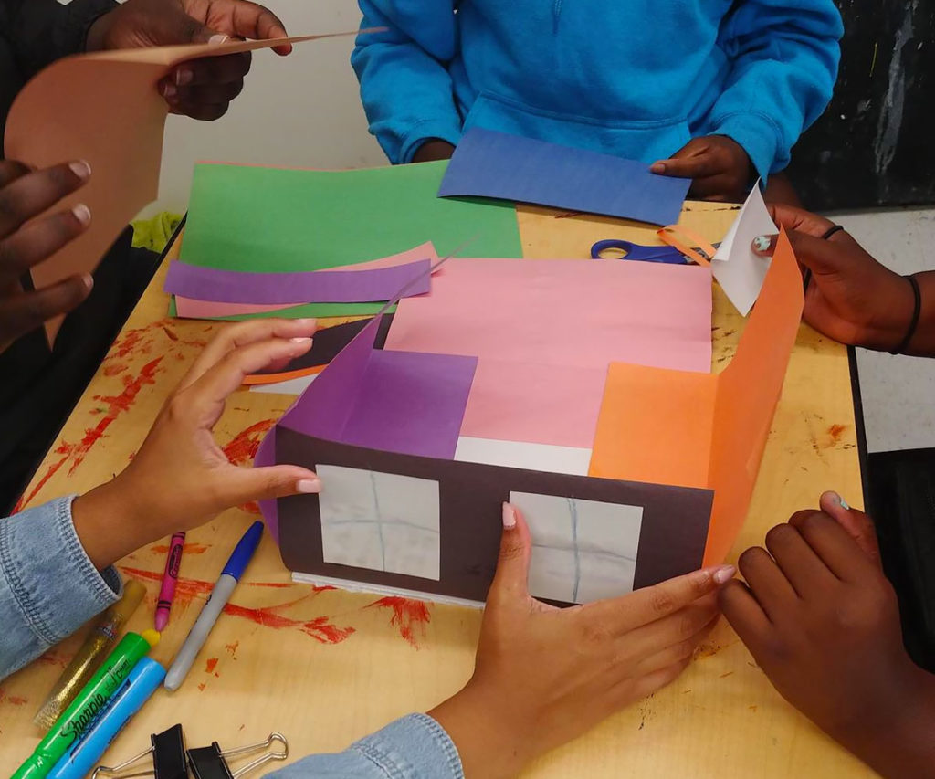 Group of girls from FYRE Initiative building paper houses