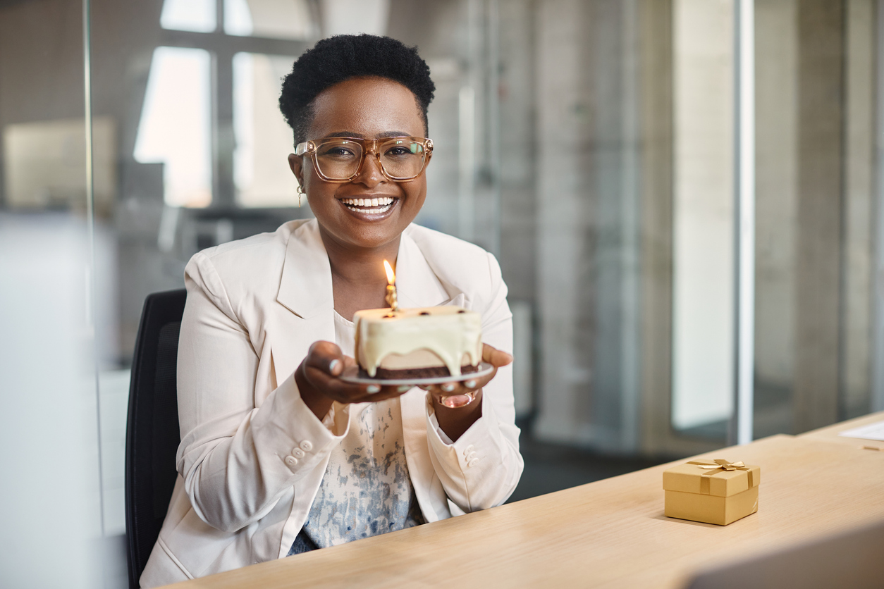 Happy African American businesswoman with her Birthday cake in the office looking at camera.